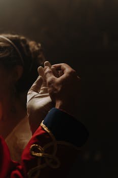 A close-up of a couple in extravagant 18th-century clothing, holding hands indoors.