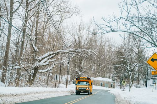 Free A yellow school bus navigates a snowy road lined with bare trees during winter. Stock Photo