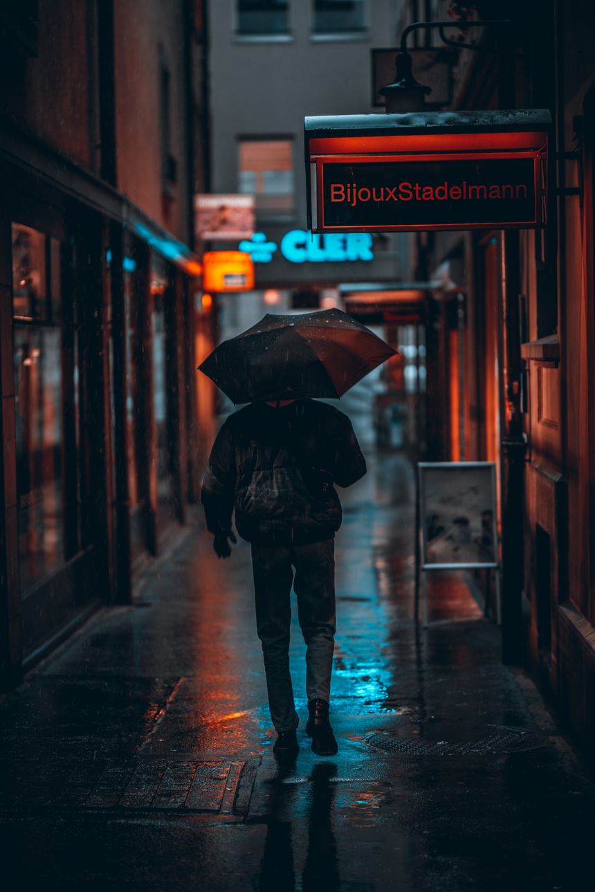Person walking with an umbrella on a rainy city street at night, by incusion on Pexels