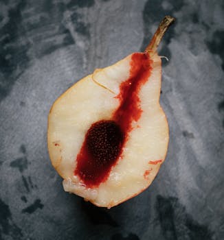 A detailed close-up of a sliced pear with a striking red center on a textured surface.