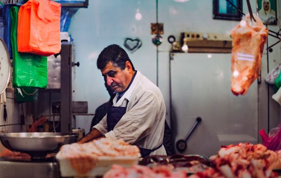 A butcher cuts meat at a market stall in Doha, Qatar, showcasing traditional butchery skills.