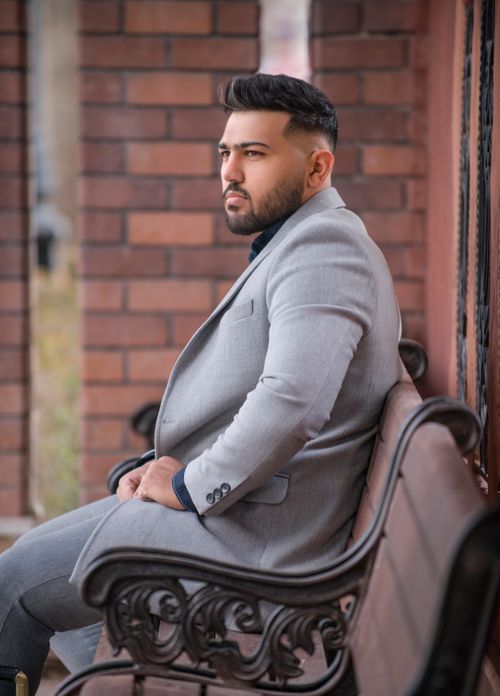 Free Fashionable man in a stylish gray suit seated on a bench outdoors, exuding elegance and confidence. Stock Photo