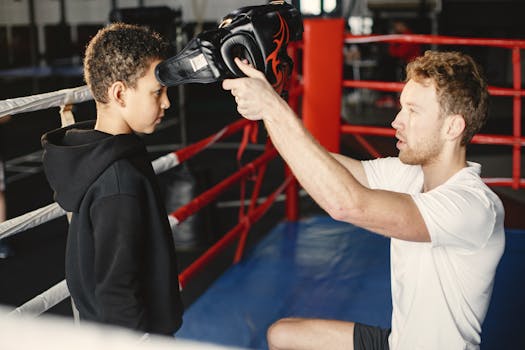 A young boy prepares for boxing practice with a trainer in a boxing gym.
