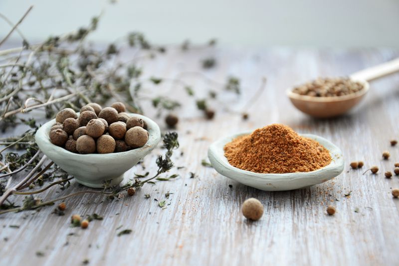 Whole and ground spices in small ceramic bowls on a pale wooden surface. Photo by Mareefe on Pexels.