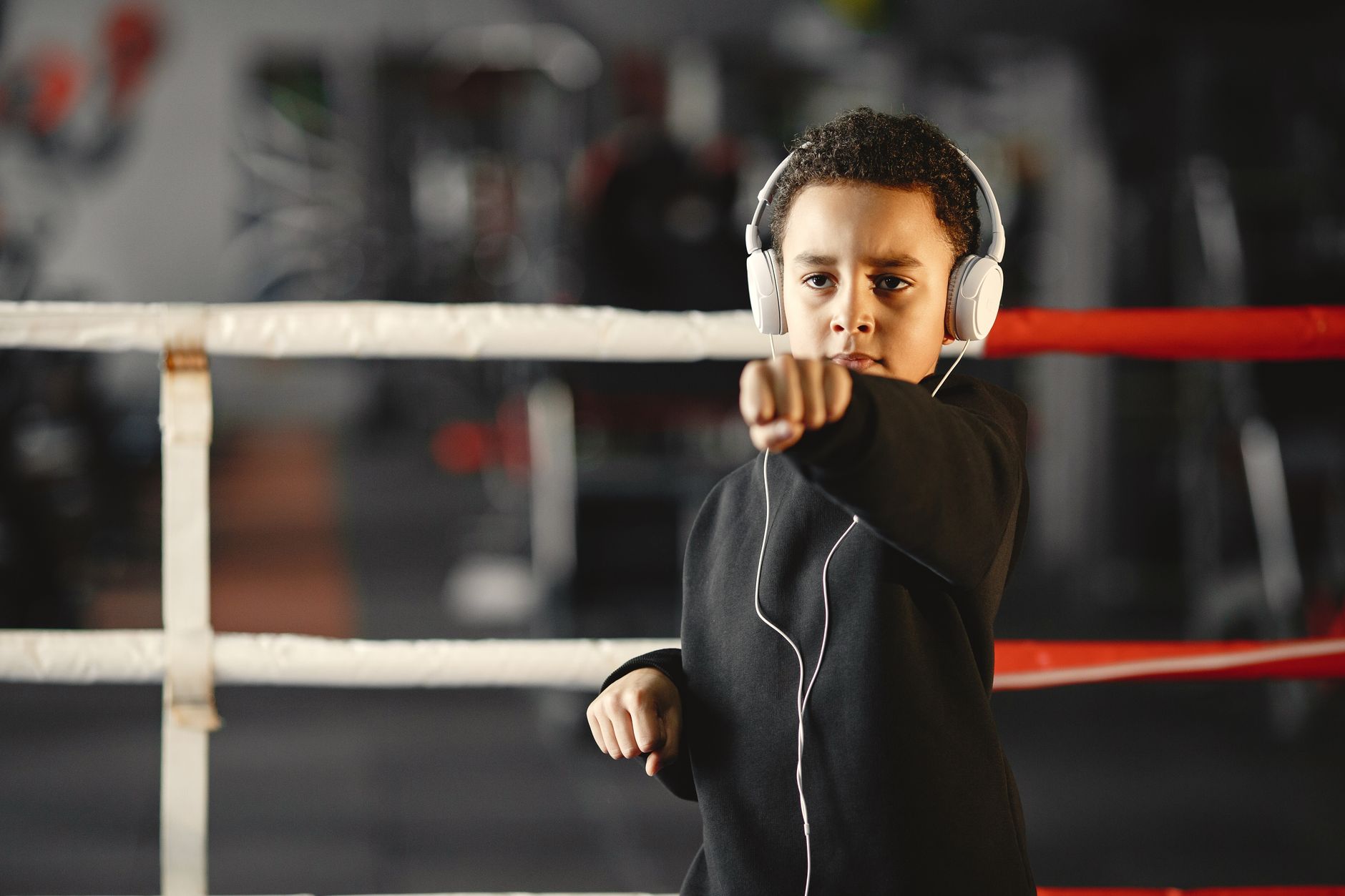 A young boy practicing boxing in a gym while wearing white headphones, focused and determined.