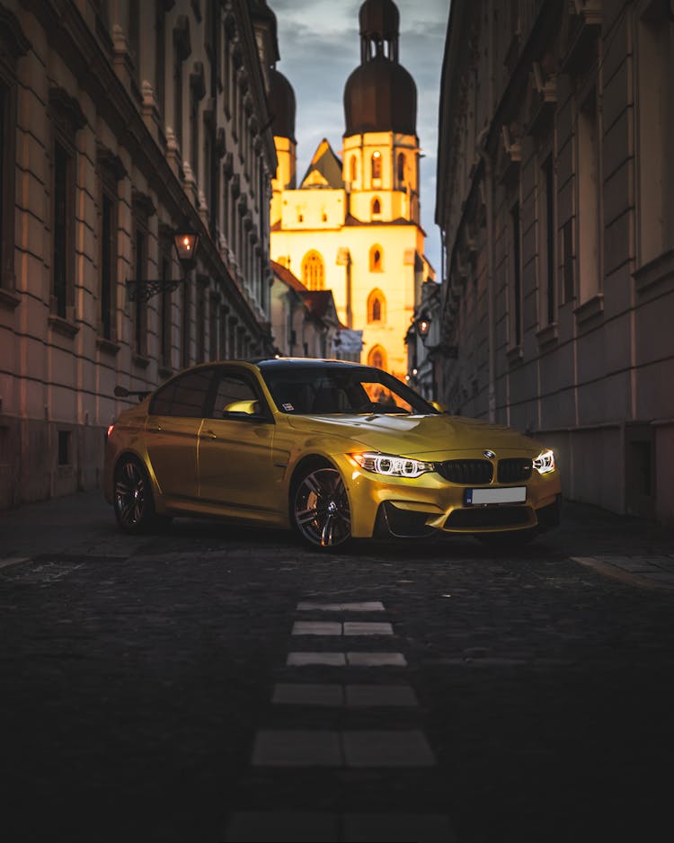 Yellow Bmw Car Parked Between Concrete Buildings 