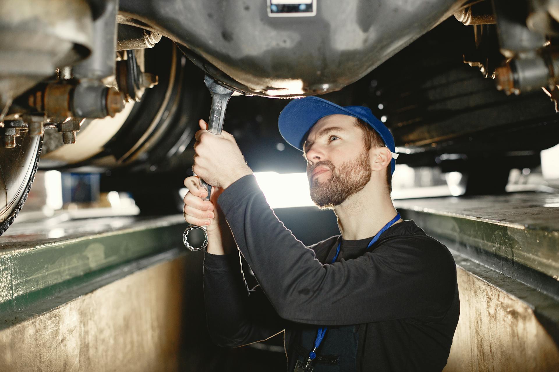 Auto mechanic repairing undercarriage in workshop with focused expression.