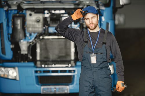 Free Auto mechanic in uniform poses confidently with truck in background. Stock Photo