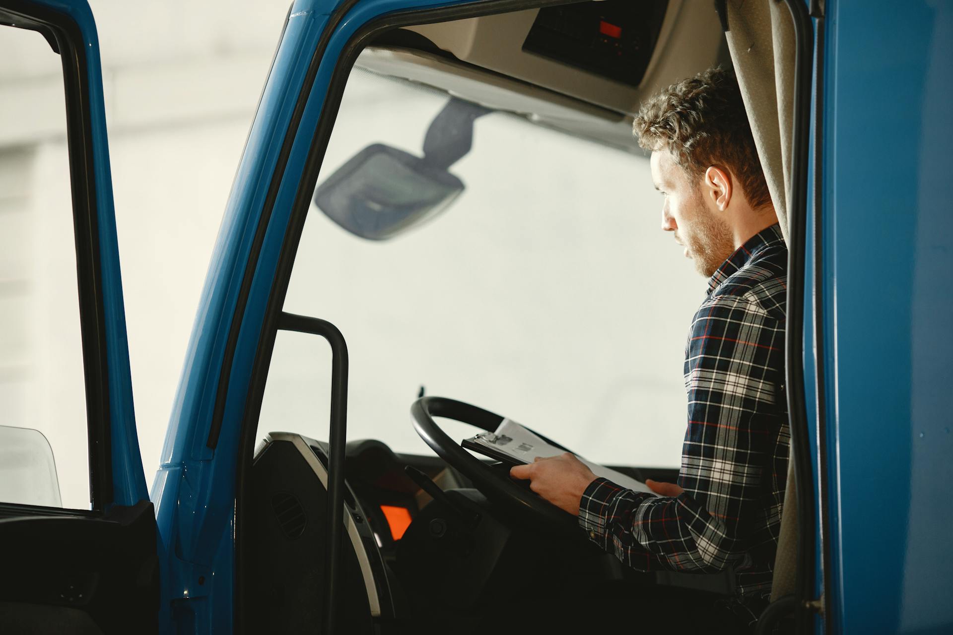 A man sitting in a truck cabin reading a document inside a blue truck, showcasing focused driving preparation.