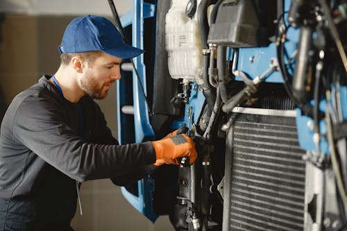 Man in Black Long Sleeve Shirt Repairing Blue Machine