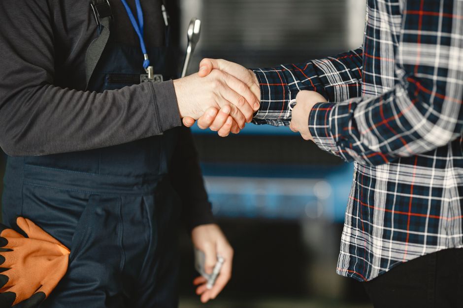 Primer plano de un apretón de manos entre trabajadores en un taller, simbolizando acuerdo empresarial y trabajo en equipo.