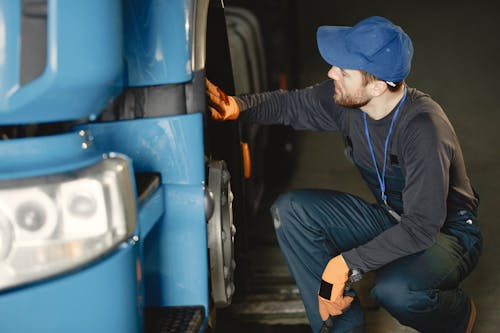 Man in Black Long Sleeve Shirt and Overall Checking Blue Truck's Wheel