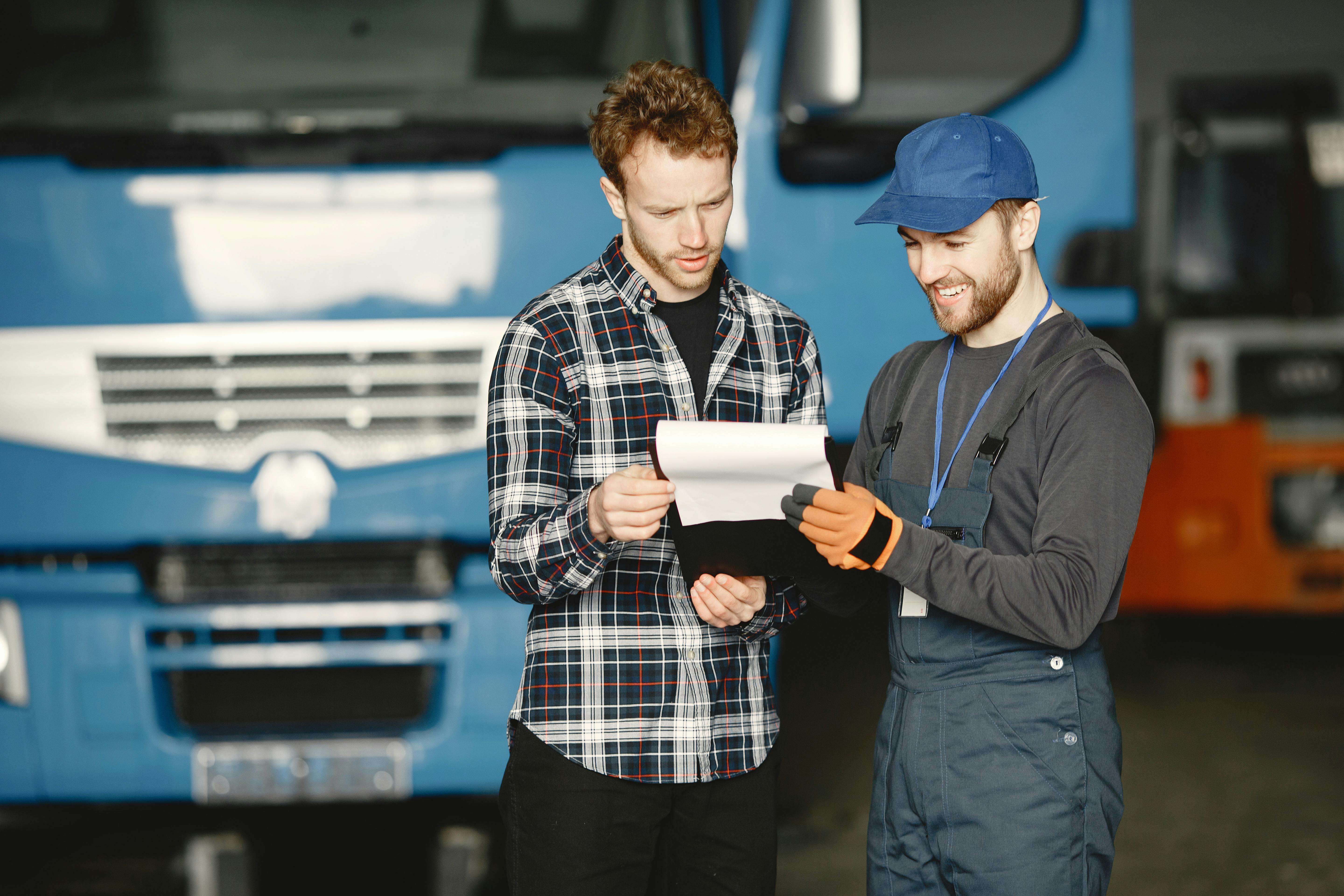 man in plaid shirt and man in working clothes looking at the papers