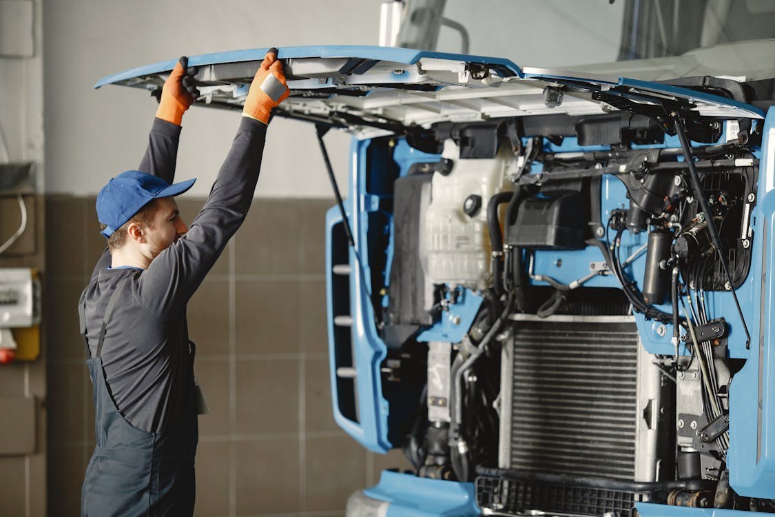 Man in working clothes inspecting the diesel engine of a blue truck