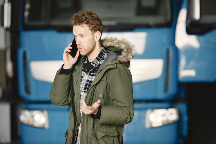 Man In Green Coat Talking On The Mobile Phone Beside Blue Truck