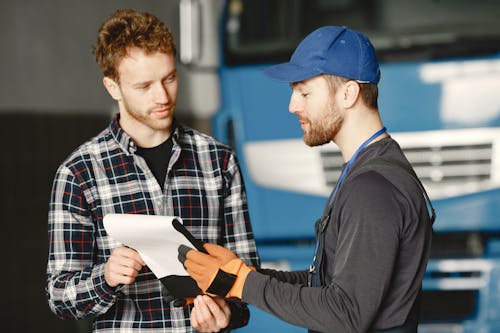 Man in Black Uniform and Blue Cap Holding White Paper Beside Man in Plaid Shirt