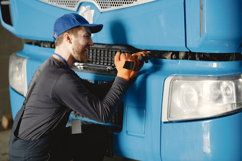 Man in Blue Cap and Orange Gloves Fixing Blue Truck