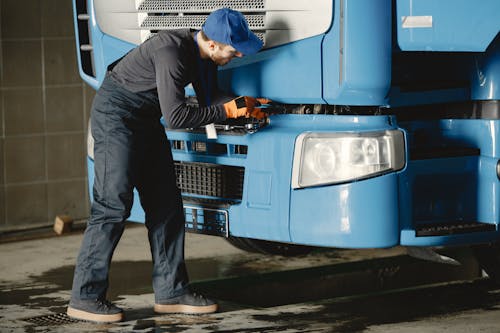 Man in Blue Cap and Working Overall Fixing Blue Truck