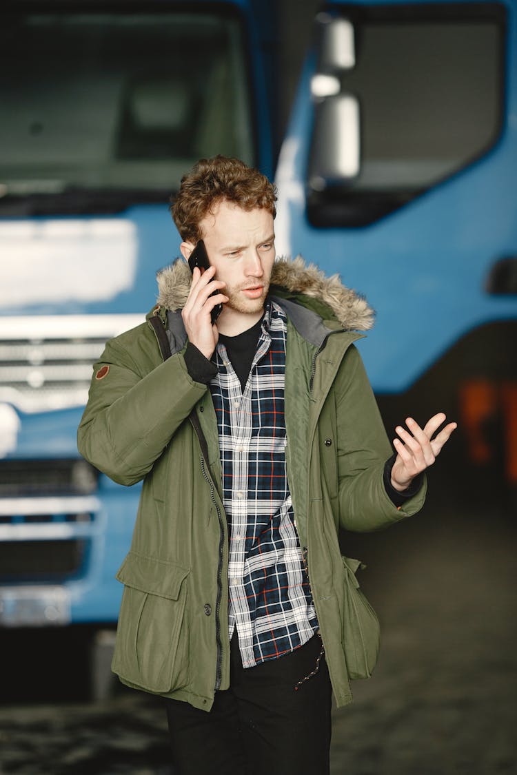 Man In Green Coat Talking On The Phone In Front Of Blue Truck