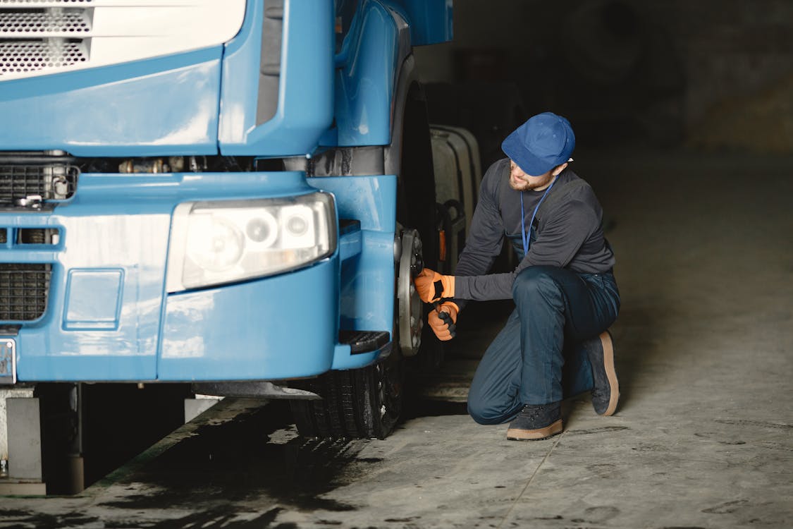 Free Man in Blue Cap Repairing Blue Truck's Wheel Stock Photo