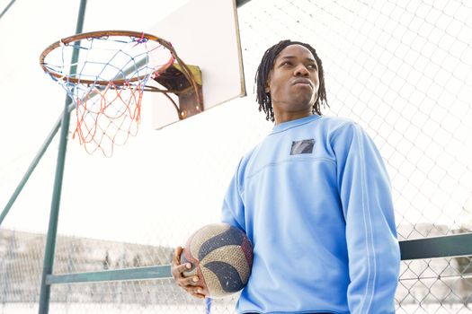 Young man playing basketball on an outdoor court holding a ball, wearing blue sleeves.