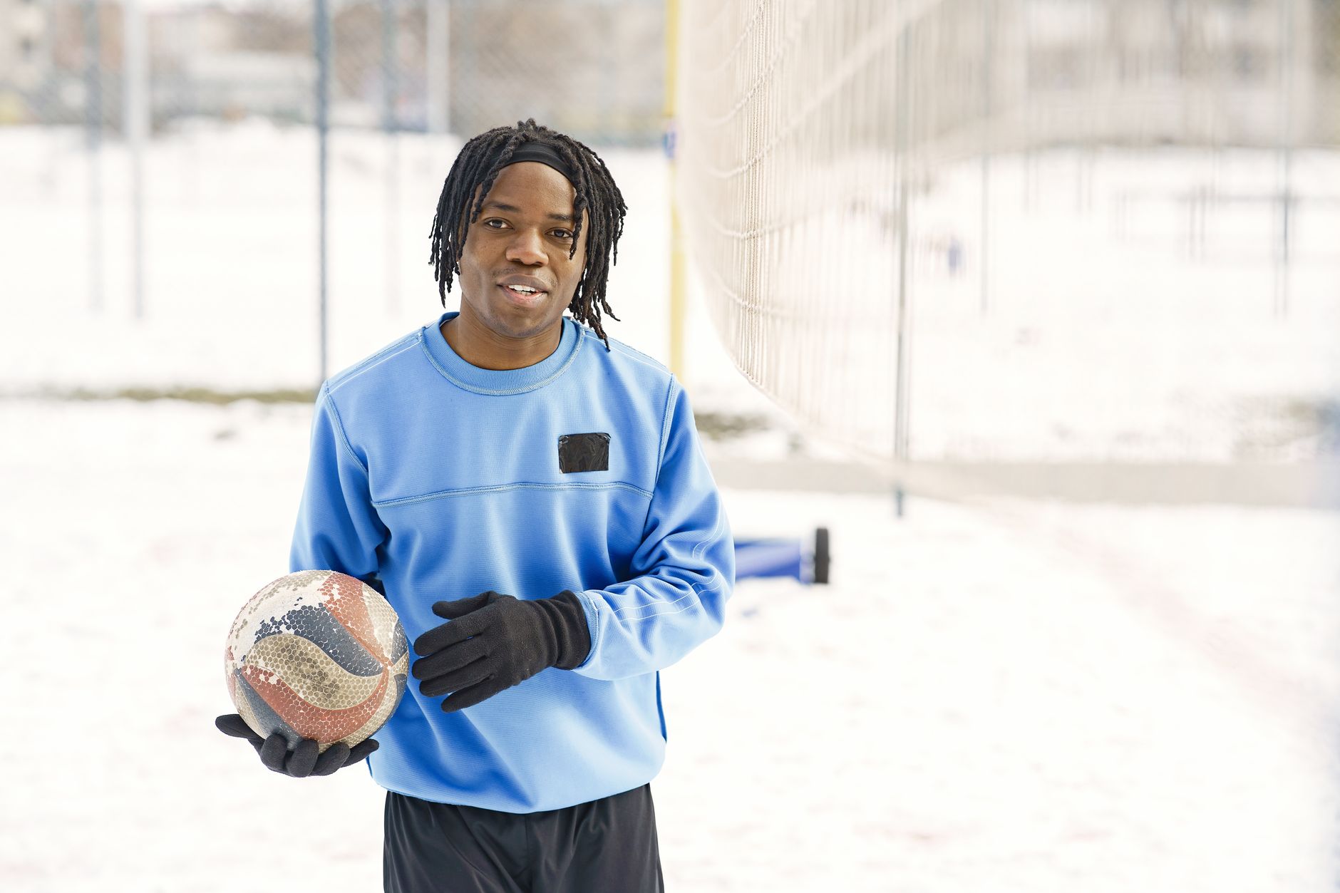A young athlete holds a volleyball outdoors on a snowy winter day, smiling warmly.