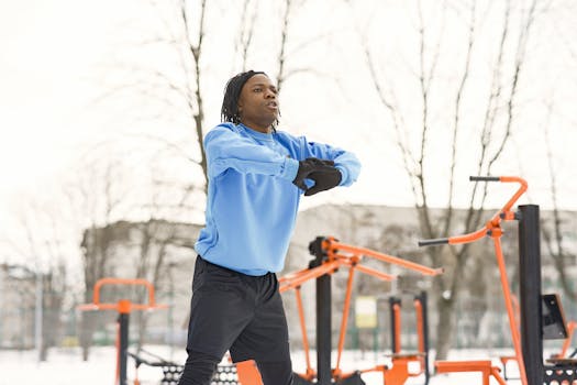 Athlete working out at an outdoor gym in wintertime, warming up in a blue sweatshirt.