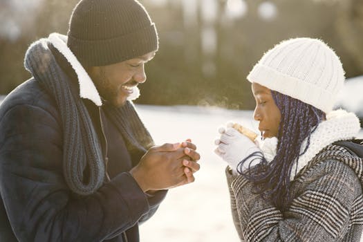 A happy couple enjoying hot beverages in snowy winter scenery.