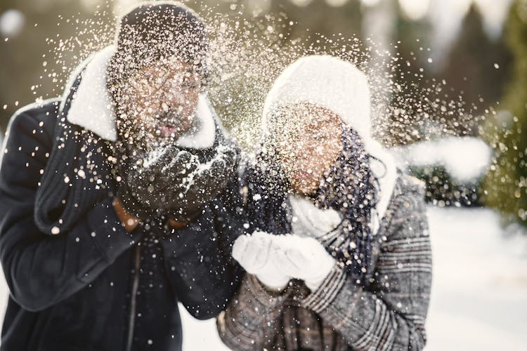 Young Couple Blowing At Snow In Their Hands 