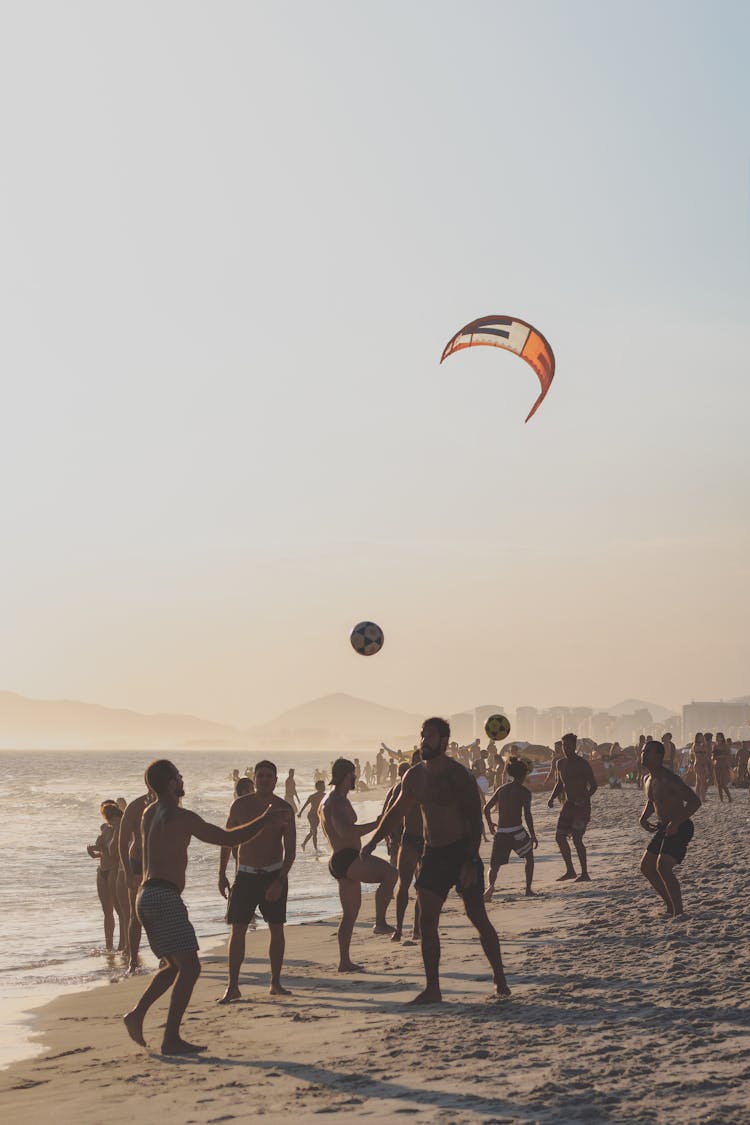 A Group Of Men Playing Football At The Beach