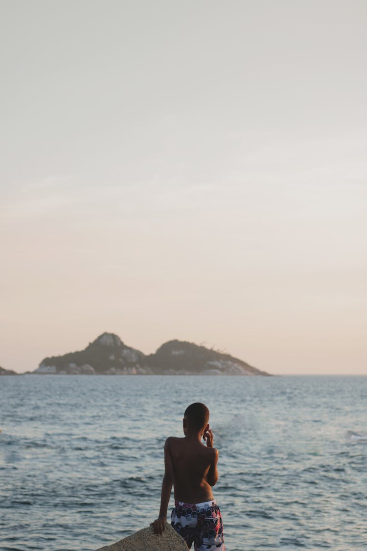 Back View Of A Boy Looking At Sea And Rock On Horizon