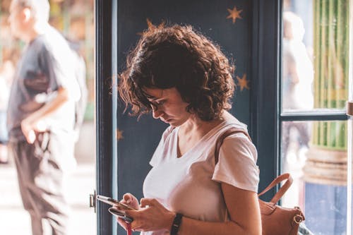 Curly Haired Woman in White T-Shirt Using her Smartphone 