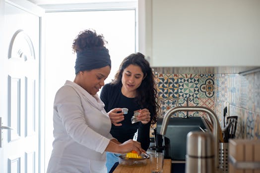 Two women preparing a citrus drink in a modern kitchen with patterned tiles, enjoying a moment together.