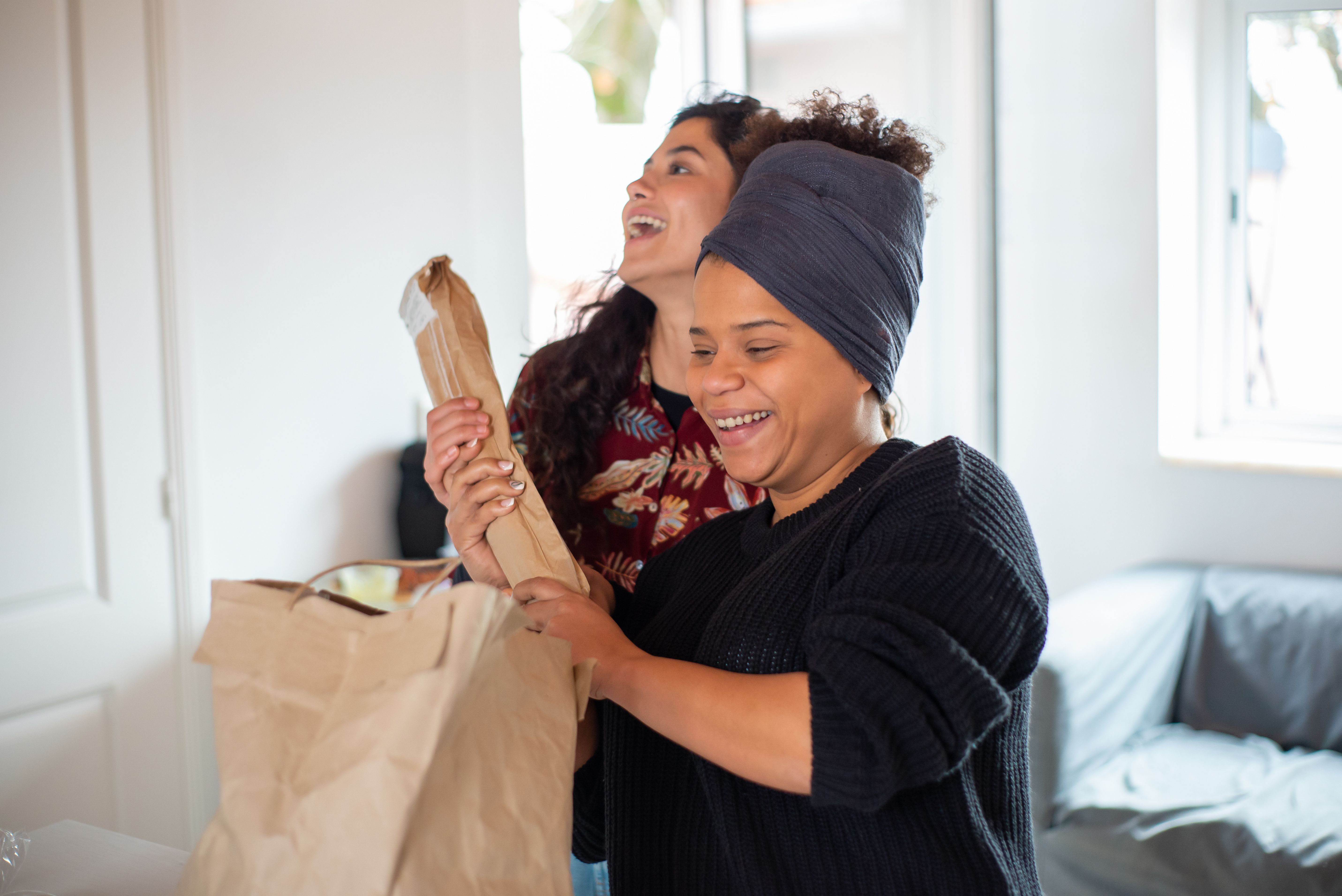Two women happily unpack groceries in a cozy kitchen setting, enjoying a leisure moment.