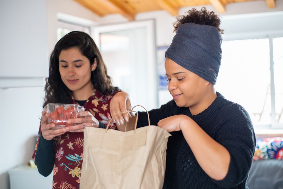 Group of young Black Nigerian friends in a Manchester living room sorting shared bags of African groceries into individual piles on the floor and sofa, warm evening light, photorealistic