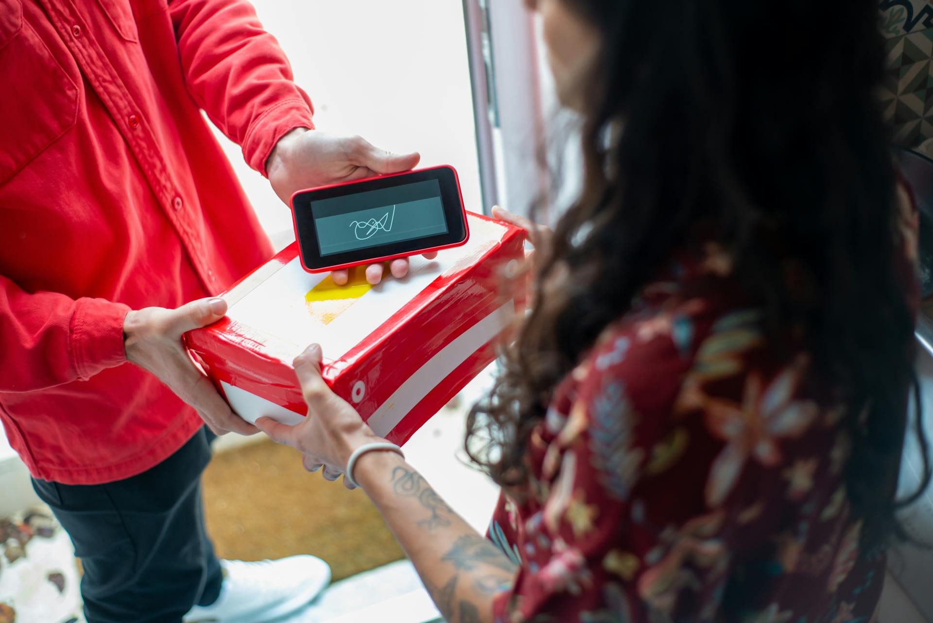 A delivery person hands over a package to a recipient using an electronic device for signature confirmation.