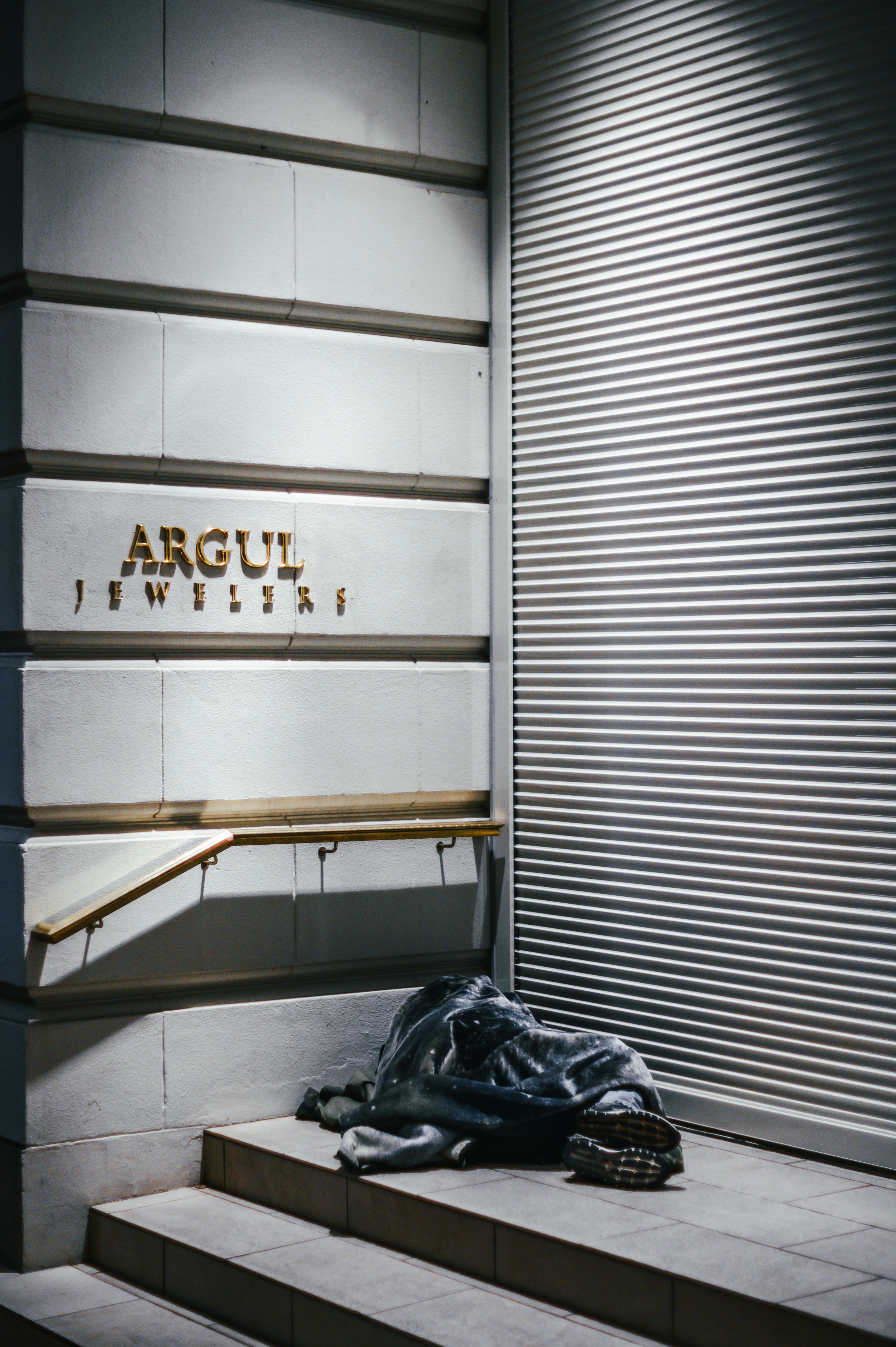 Full body of anonymous homeless person covered with blanket sleeping on stairs of modern building on street in evening time