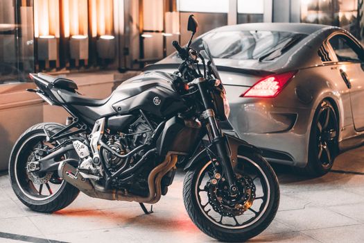 Sleek black motorcycle and luxury car parked in a stylish garage setting, showcasing elegance and performance.