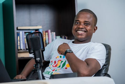 African American man smiling while podcasting at home studio with microphone and books.