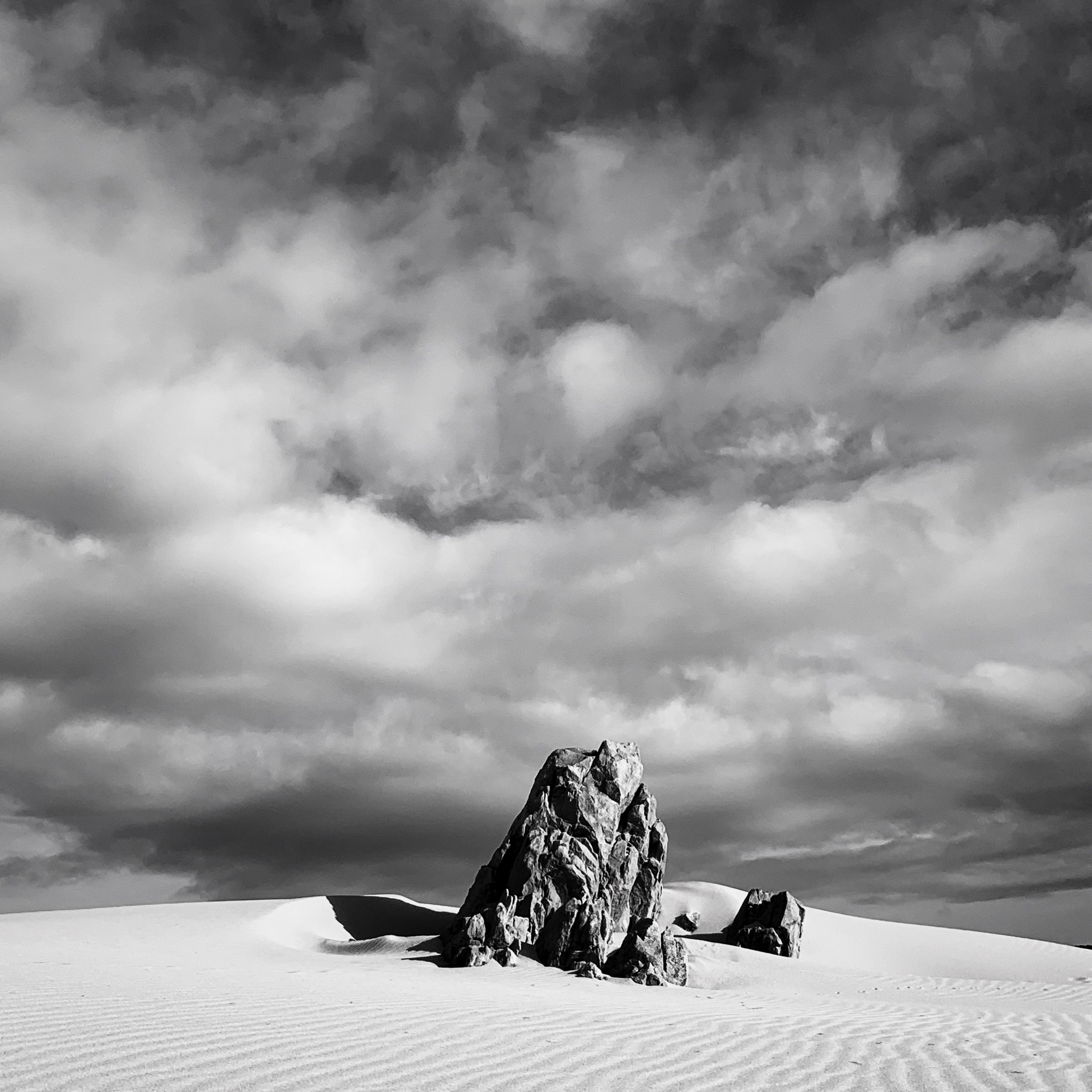 A striking black and white photo of a rock formation under dramatic clouds in a barren desert.