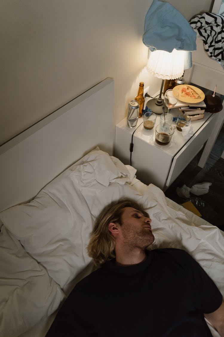 Man Lying In Bed Next To Cluttered Nightstand