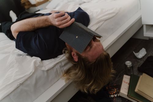 Free A man lying on a bed with a book covering his face, capturing a moment of relaxation. Stock Photo