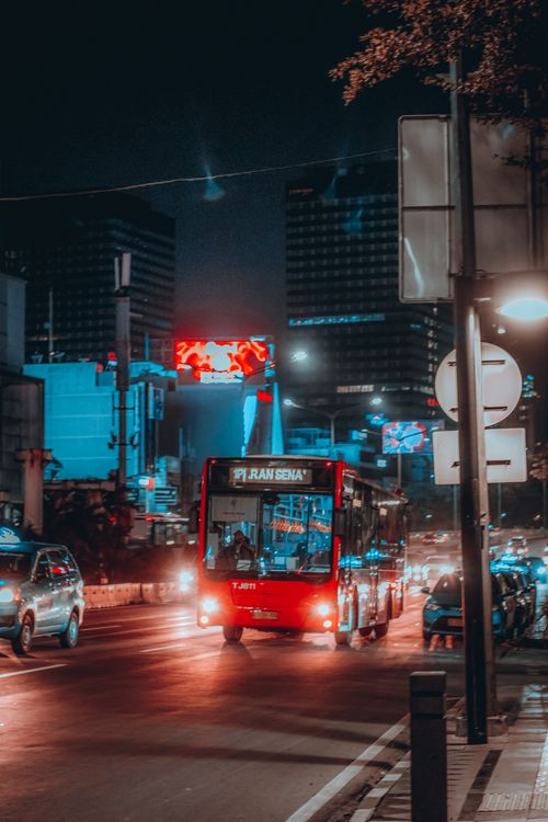 Free Vibrant urban scene featuring an illuminated red bus navigating city traffic at night. Stock Photo