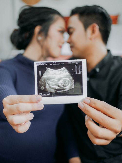 Free Couple lovingly holding and showing a pregnancy ultrasound photo, smiling in anticipation. Stock Photo