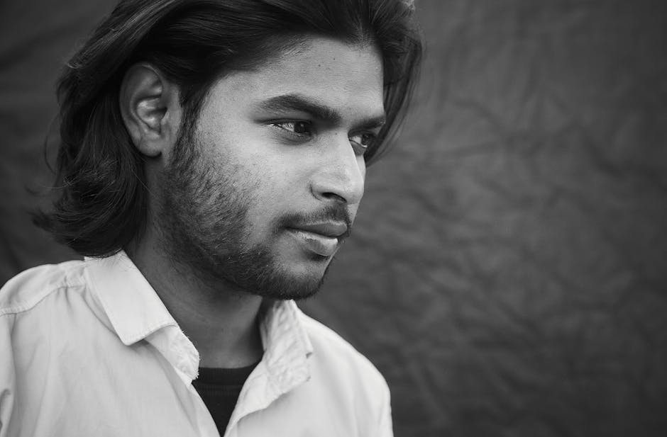 Grayscale close-up of a contemplative man with facial hair, wearing a collared shirt.