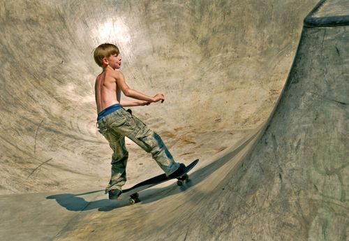 Free A young boy demonstrates skateboarding skills in a concrete skatepark bowl on a sunny day. Stock Photo