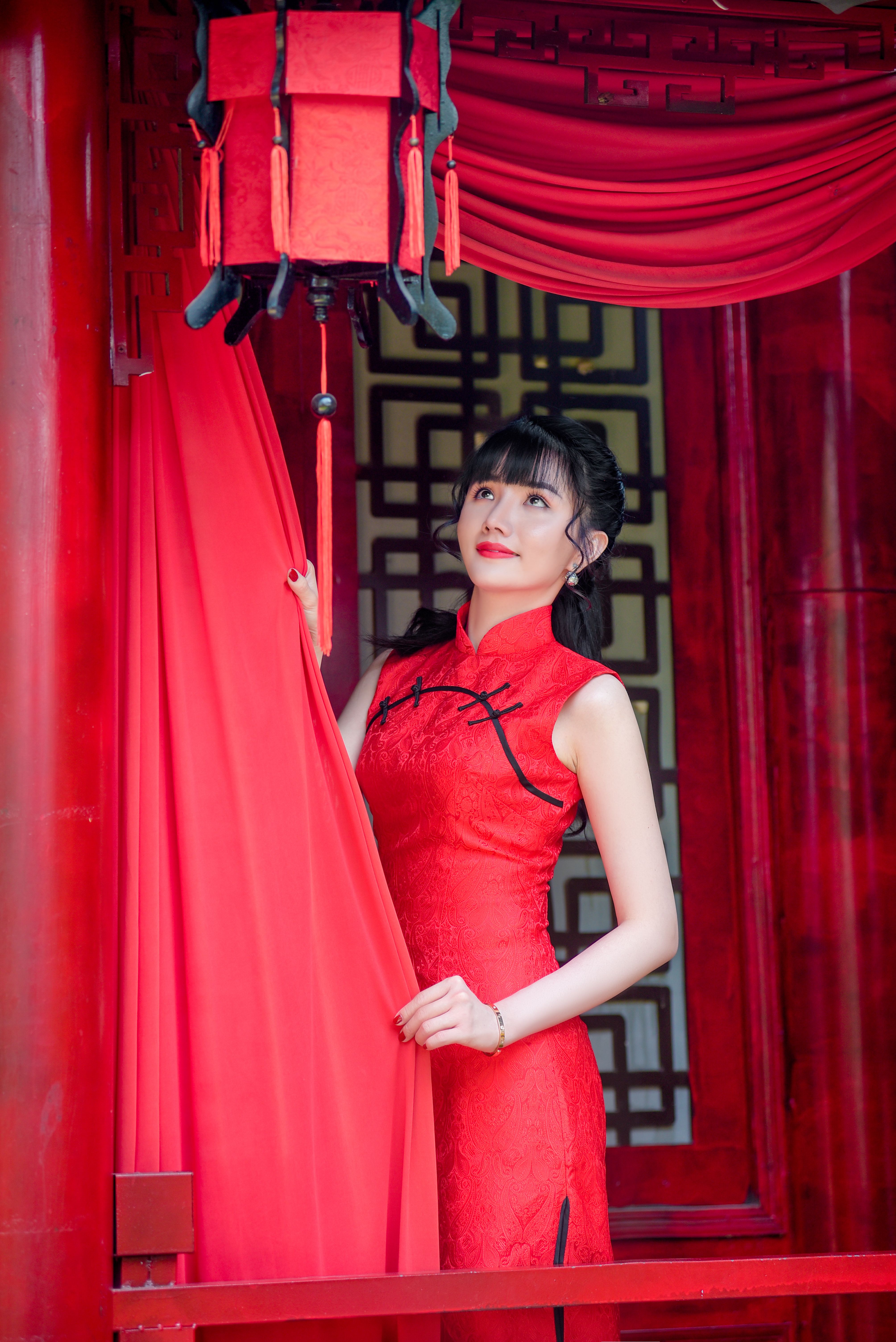 Asian woman in a stunning red cheongsam dress gazes thoughtfully indoors.