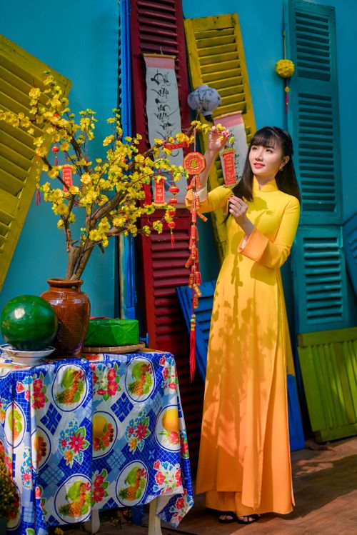 Free Woman in yellow áo dài decorates for Tet with vibrant flowers and ornaments. Stock Photo