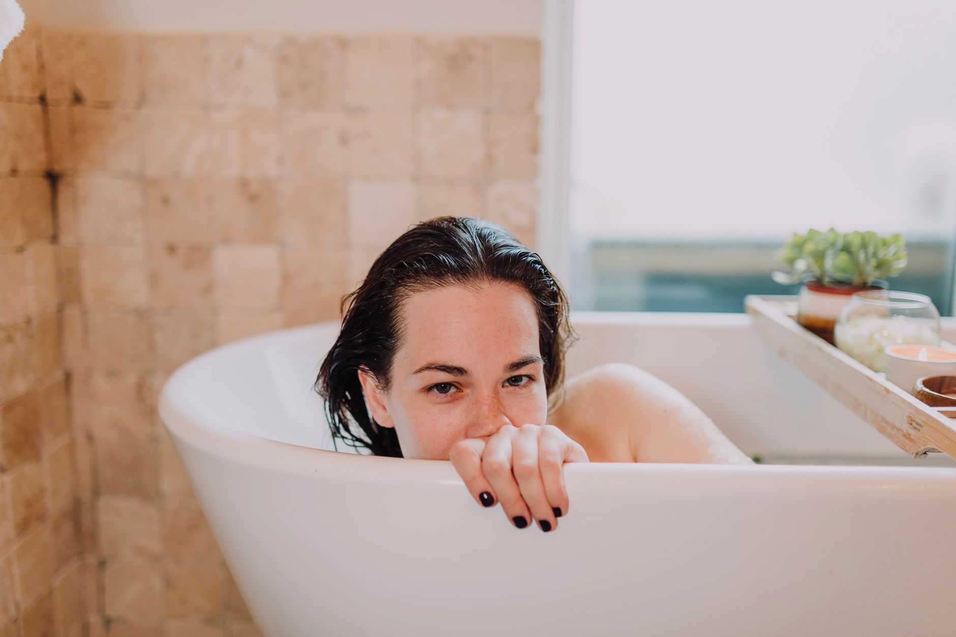 A woman enjoys a peaceful bath with spa essentials and candles around for a calming experience.