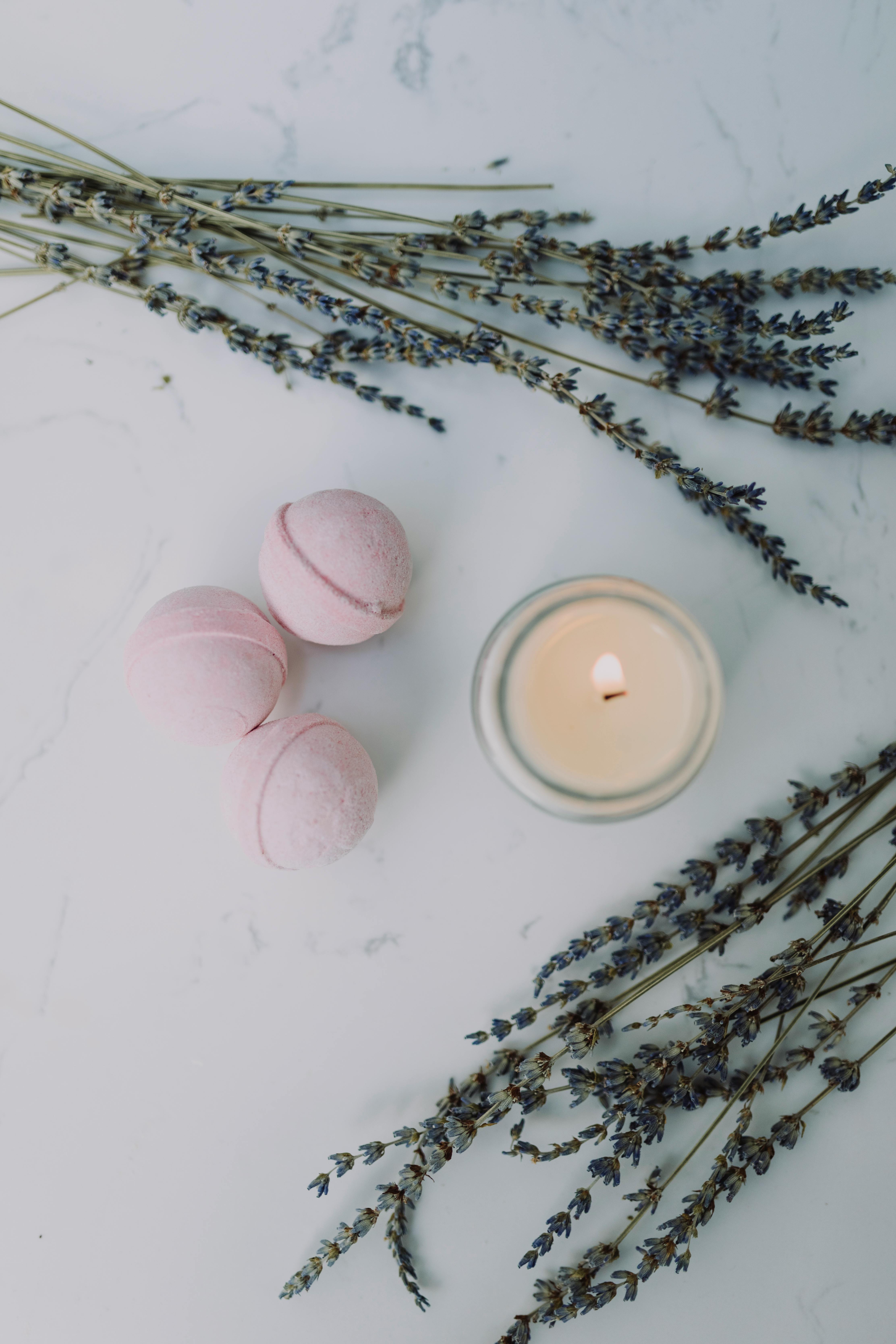 Top view of bath bombs, lavender sprigs, and a lit candle on a marble surface, perfect for a relaxing spa day.